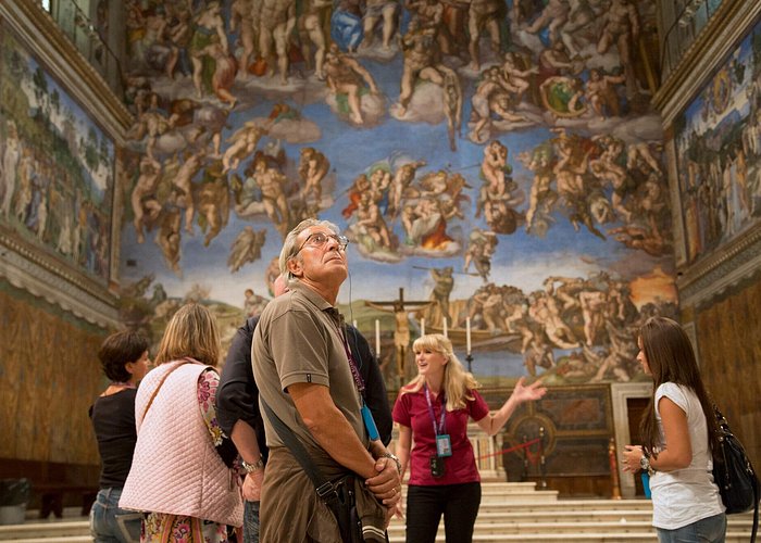 Group of people in a museum observing a large frescoed ceiling.